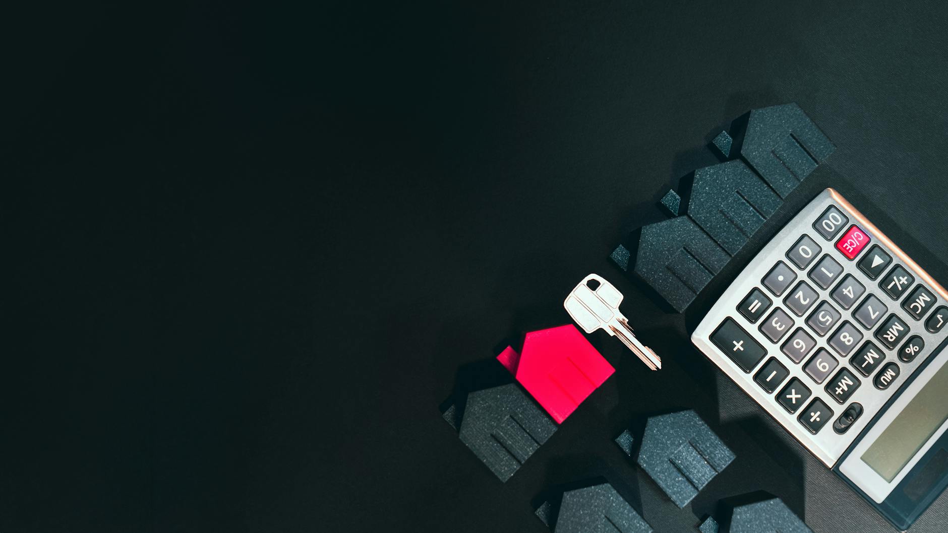 Kalkulator, miniaturowe domy i klucz symbolizujące inwestycje w nieruchomości