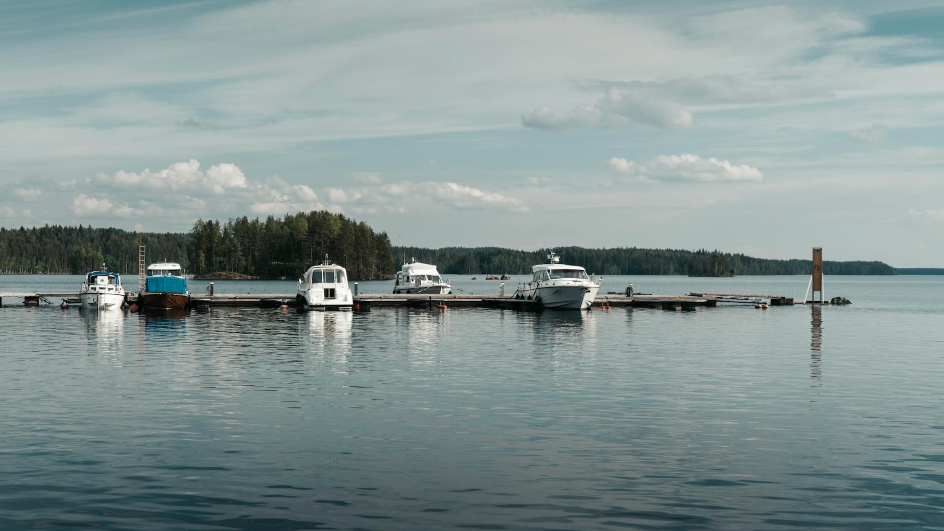 Łodzie zacumowane w spokojnej marinie nad fińskim jeziorem wśród lasów